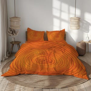 May include: An orange and yellow bedding set featuring a tree ring design. The set includes a comforter and two pillowcases. The bedding is displayed on a bed with a wooden headboard and a round, woven rug.