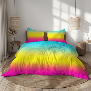 Op de afbeelding: Een bed met een levendige, kleurrijke beddenset. Het dekbed en de kussenslopen hebben een gradiëntontwerp, dat overgaat van roze naar geel en blauw. Het bed staat op een ronde, geweven vloerkleed, met een neutrale inrichting op de achtergrond.