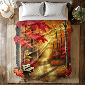 Könnte beinhalten: Eine Decke mit einem Gemälde eines Waldweges im Herbst. Der Weg ist gesäumt von Bäumen mit roten, orangefarbenen und gelben Blättern. Eine Holzbank steht auf dem Weg.