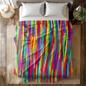 Pode incluir: Um cobertor colorido com um padrão vibrante de listras verticais em tons de vermelho, amarelo, verde, azul e roxo. O cobertor está sobre uma cama com travesseiros brancos, criando uma estética brilhante e alegre. O design do cobertor adiciona um toque moderno ao quarto.