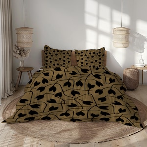 May include: A bed set featuring a duvet cover and two pillowcases. The bedding has a tan background with a repeating pattern of black leaf-like shapes. The bed is made up with a wooden headboard and is on a round, woven rug.