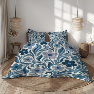 May include: A blue and white floral patterned bedding set. The set includes a duvet cover and two pillowcases. The design features stylized flowers and leaves in shades of blue and light blue against a cream background. The bedding is on a bed with a wooden headboard.