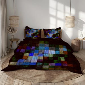 Op de afbeelding: Een bed met een donkerbruin dekbedovertrek en twee kussenslopen. Het beddengoed heeft een kleurrijk, geometrisch patroon van vierkanten in tinten blauw, groen, rood en oranje. Het bed staat op een rond, geweven tapijt.