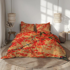 Puede incluir: Un juego de cama que incluye una funda nórdica y dos fundas de almohada a juego con un diseño estampado de hojas de arce rojas vibrantes sobre ramas en un fondo color canela claro, con pequeños pájaros azules posados en las ramas.