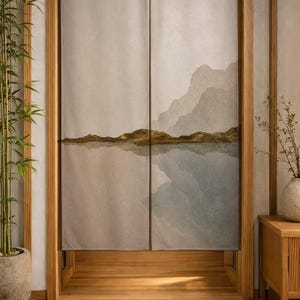 Peut inclure: Un rideau noren en tissu divisé en deux panneaux présentant un paysage imprimé de montagnes gris sourd et une ligne d'horizon brun doré se reflétant dans l'eau, suspendu dans un cadre de porte en bois avec un sol en tatami et des bambous.