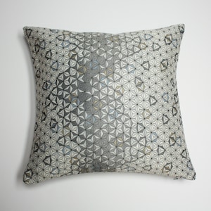 May include: A decorative throw pillow with a geometric pattern in shades of gray, white, and blue. The pattern is made up of small stars.