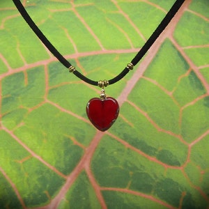 May include: A red glass heart pendant necklace on a black cord with gold beads.