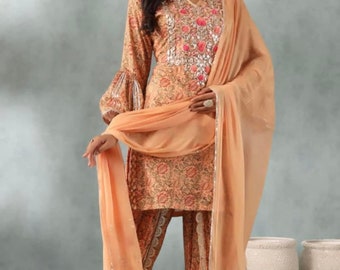 May include: A peach-colored salwar kameez with a floral print and silver embroidery. The outfit includes a long-sleeved top, pants, and a matching dupatta.