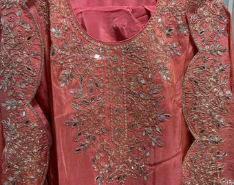 May include: Coral-colored formal wear with intricate embroidery and mirror work. The long-sleeved garment features a round neckline and detailed embellishments along the sleeves and bodice, creating a luxurious and ornate appearance. The fabric has a subtle sheen.