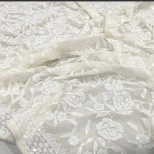 May include: White sheer fabric with a floral pattern made of white sequins. The fabric is delicate and has a soft, flowing texture.