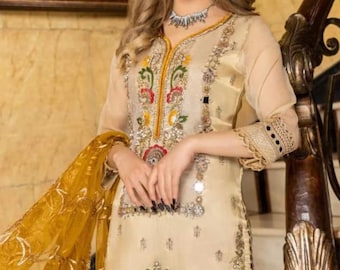 May include: A cream-colored embroidered dress with gold and silver embellishments, a red and gold dupatta, and a matching red bottom. The dress features a V-neckline and three-quarter sleeves.