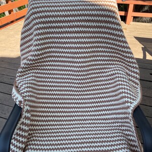 May include: A brown and white striped crocheted throw blanket is draped over a black chair on a wooden deck.