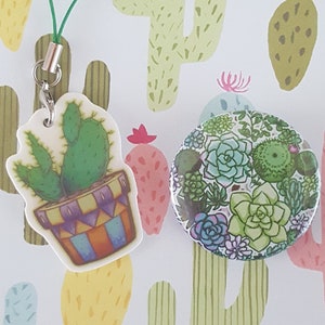 May include: A green and white cactus charm with a green string attached. The charm is on a white background with a pattern of colorful cacti.