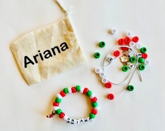 May include: A white drawstring bag with the name "Ariana" printed on it.  A red, white, and green beaded bracelet with the name "Ariana" spelled out in white letter beads.  The bracelet is next to a pile of red, white, and green beads.