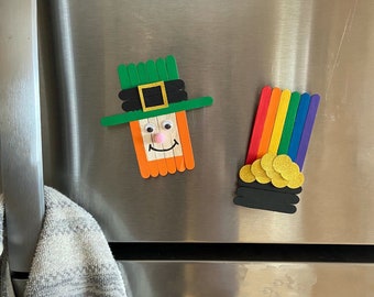 May include: A green, white, and orange leprechaun craft made from popsicle sticks, with a black hat and a smiling face. A rainbow and gold coin craft made from popsicle sticks is also shown.
