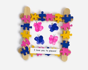 May include: A handmade picture frame made from popsicle sticks and decorated with colorful puzzle pieces. The frame contains a white card with hand-painted butterflies and the text "I love you to pieces!"