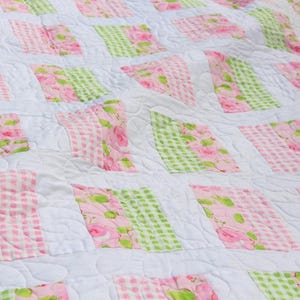 May include: A white quilt with a patchwork design featuring pink and green floral fabric. The quilt is quilted with a swirl pattern.