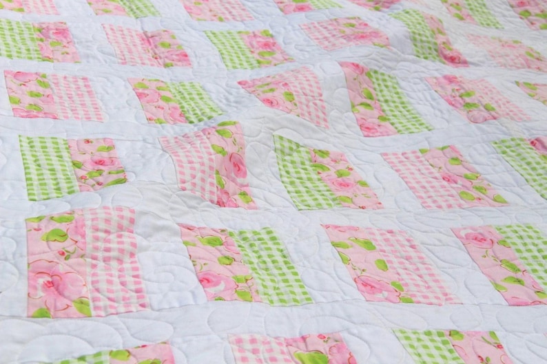 May include: A white quilt with a patchwork design featuring pink and green floral fabric. The quilt is quilted with a swirl pattern.