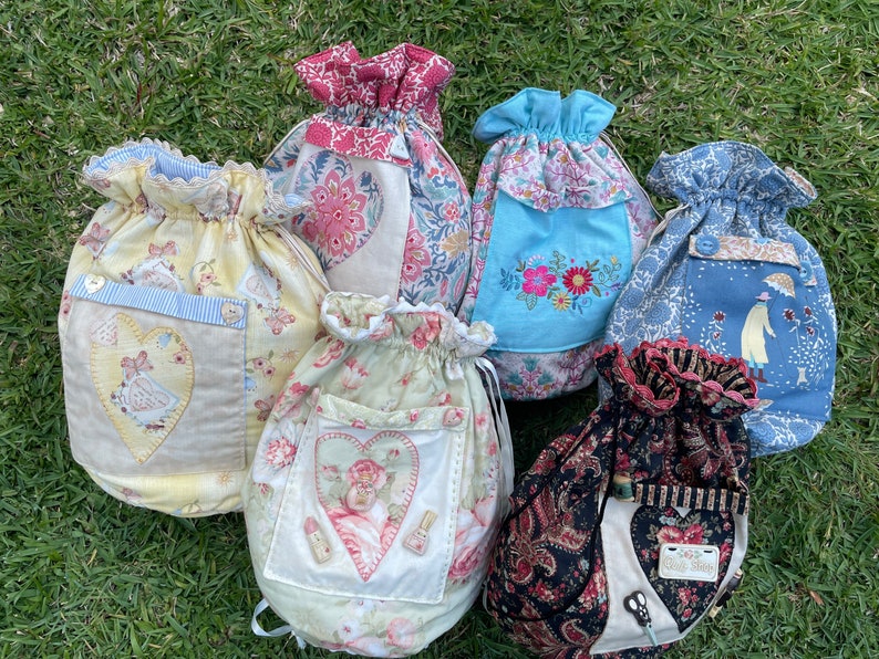 May include: Six drawstring bags made of fabric with various floral patterns and designs. The bags have a heart-shaped pocket on the front and are decorated with embroidery and appliques.