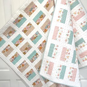 May include: Two handmade quilts with a white background and rectangular blocks of various floral and patterned fabrics in shades of blue, pink, and beige. The quilts are displayed on a white door.