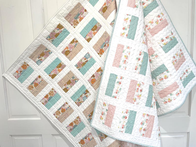 May include: Two handmade quilts with a white background and rectangular blocks of various floral and patterned fabrics in shades of blue, pink, and beige. The quilts are displayed on a white door.