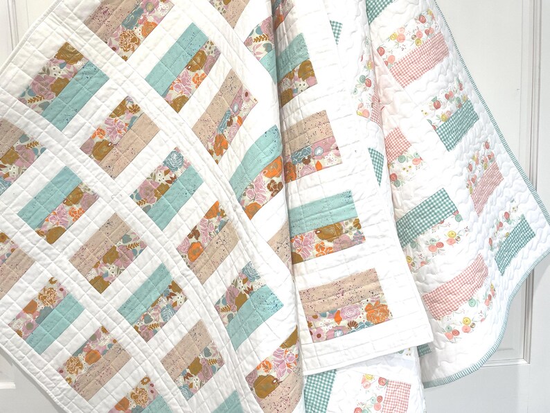 May include: A handmade quilt with a white background and a patchwork design. The quilt features rectangular blocks in shades of blue, tan, and floral patterns. The quilt is made of soft fabric and has a quilted texture.