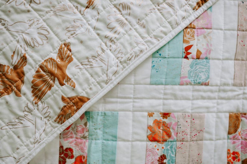 May include: A patchwork quilt with a cream-colored background. One section features brown bird illustrations, while the other has floral and striped patterns in pink, orange, and blue. The quilt is quilted with a diamond pattern.