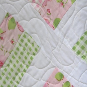 May include: A patchwork quilt with a white background and pink and green floral patterns. The quilt is quilted with a wavy stitch pattern.