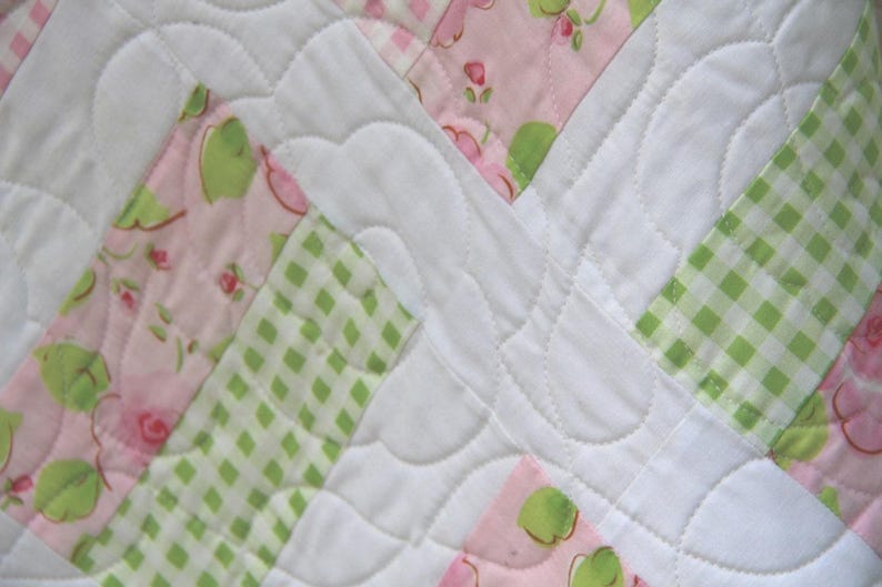 May include: A patchwork quilt with a white background and pink and green floral patterns. The quilt is quilted with a wavy stitch pattern.