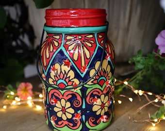 May include: A colorful ceramic lantern with a red, blue, yellow, and green geometric pattern. The lantern has a black metal handle and is decorated with stars and flowers.