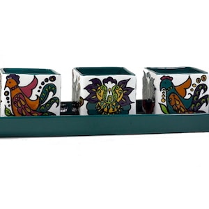 Könnte beinhalten: Drei kleine, quadratische Keramik-Blumentöpfe mit bunten Vogel- und Blumendesigns, die auf einem türkisfarbenen Tablett stehen.