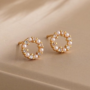 May include: A pair of gold earrings with a circle design. The circle is made of small pearls and clear rhinestones.