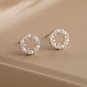 May include: A pair of silver stud earrings with a circle design. The circle is made of small white pearls.