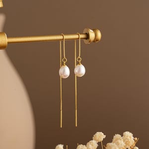 May include: A pair of gold chain earrings with a white pearl dangling from each chain.