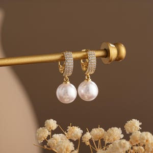 May include: Gold hoop earrings with a pearl drop. The hoops are encrusted with small clear stones.