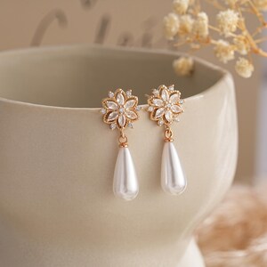 Peut inclure: Boucles d'oreilles dorées avec une goutte nacrée et un motif floral avec des strass transparents.