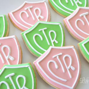 May include: A close-up of several decorated sugar cookies in the shape of shields. The cookies are decorated with green and pink icing and the letters "CTR" in white icing.