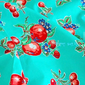 May include: A vibrant turquoise fabric featuring a repeating pattern of bright red cherries, strawberries, and small blue flowers with green leaves. The design includes clusters of fruit and foliage scattered across the surface in a consistent layout.