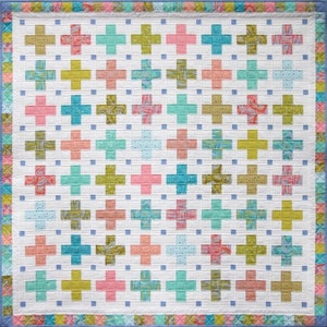 May include: A patchwork quilt featuring a repeating cross design in various colours, including pink, teal, and green, set against a white background. The quilt has a patterned border and is likely made of cotton.