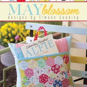 May include: A patchwork cushion with a pocket containing a book titled "Alfie's Feet" by Shirley Hughes. The cushion is decorated with a variety of colourful floral and patterned fabrics. The image includes a banner with the text "MAY blossom designs by Simone Gooding".