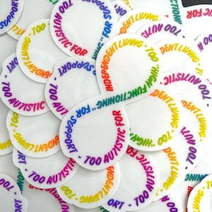 May include: A close-up of a pile of round white stickers with rainbow colored text that reads "Too Autistic For..." and "Independent Living - Too Autistic For High Functioning".
