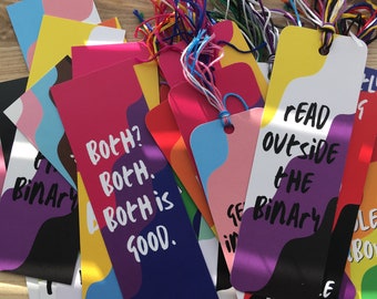 May include: A collection of colorful bookmarks with different messages. The bookmarks feature abstract shapes and designs with a rainbow color scheme. The text on the bookmarks reads "Both? Both. Both is good." and "Read outside the binary. Books."