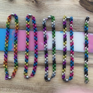 Peut inclure: Six colliers et un bracelet en cotte de mailles colorés sont présentés. Les colliers présentent une variété de couleurs, dont arc-en-ciel, rose, noir, vert et bleu. Chaque collier a un fermoir magnétique argenté. Le bracelet est une version plus petite des colliers.