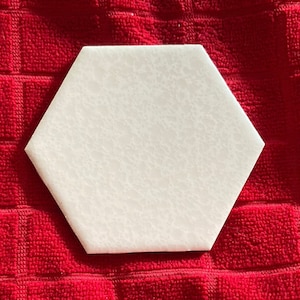 May include: A white hexagonal tile on a red kitchen towel with a waffle weave pattern.