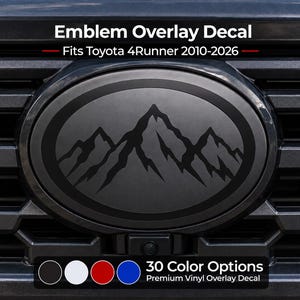 Op de afbeelding: Een ovale embleem-overlaysticker voor een Toyota 4Runner 2010-2026, met een zwarte berggrafiek op een matte donkere achtergrond. De tekst luidt Emblem Overlay Decal, Fits Toyota 4Runner 2010-2026, 30 Color Options, Premium Vinyl Overlay Decal.