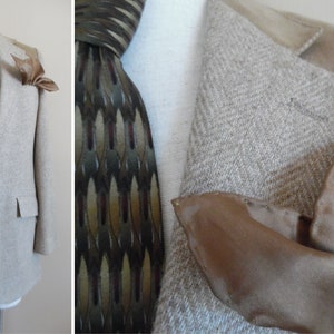 Puede incluir: Una chaqueta de punto beige con estampado de espiga, cuello de ante marrón y botones marrones. La chaqueta tiene una corbata marrón con estampado y un pañuelo de bolsillo marrón.