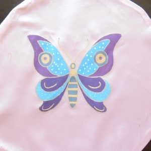 Peut inclure: Un cercle en tissu rose avec un motif de papillon peint. Le papillon a des accents violets, bleus et dorés.