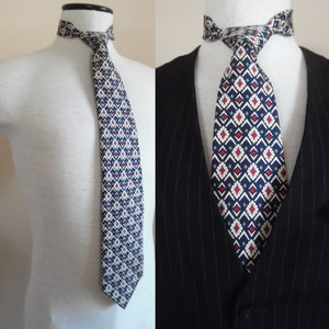 Puede incluir: Una corbata con estampado geométrico azul, blanco y rojo. La corbata está atada alrededor del cuello de un maniquí blanco y también se muestra en una chaqueta de traje de rayas finas negras.