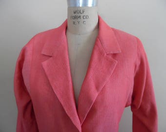 May include: A coral pink blazer with a notched collar and long sleeves. The blazer is made of a textured fabric and has a single button closure. The label on the blazer reads "Wolf Form Co. N.Y.C."