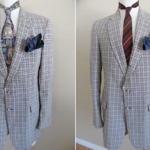 May include: A tailored blazer with a blue, white, and brown plaid pattern. The jacket features a navy blue pocket square and is paired with a patterned tie. The blazer has a classic two-button closure and notched lapels.